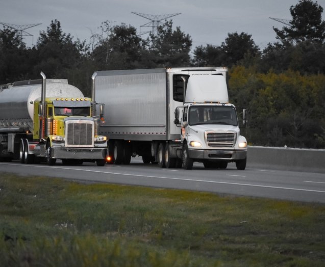 Two trailer trucks driving on the road surrounded by beautiful green trees